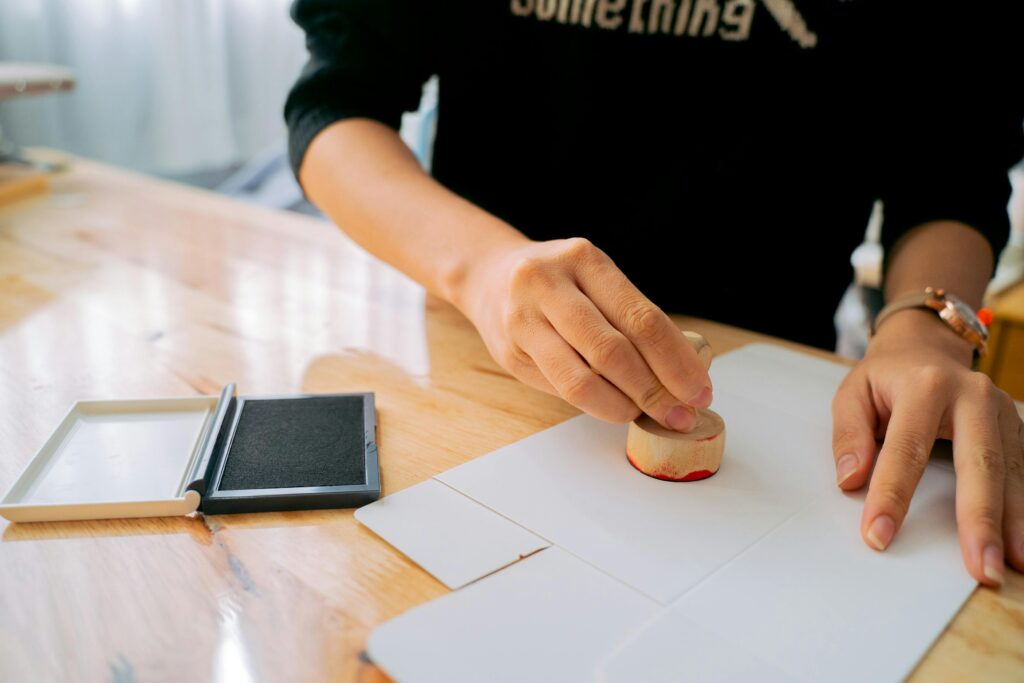 Close-up of hands stamping a document on a wooden desk indoors.